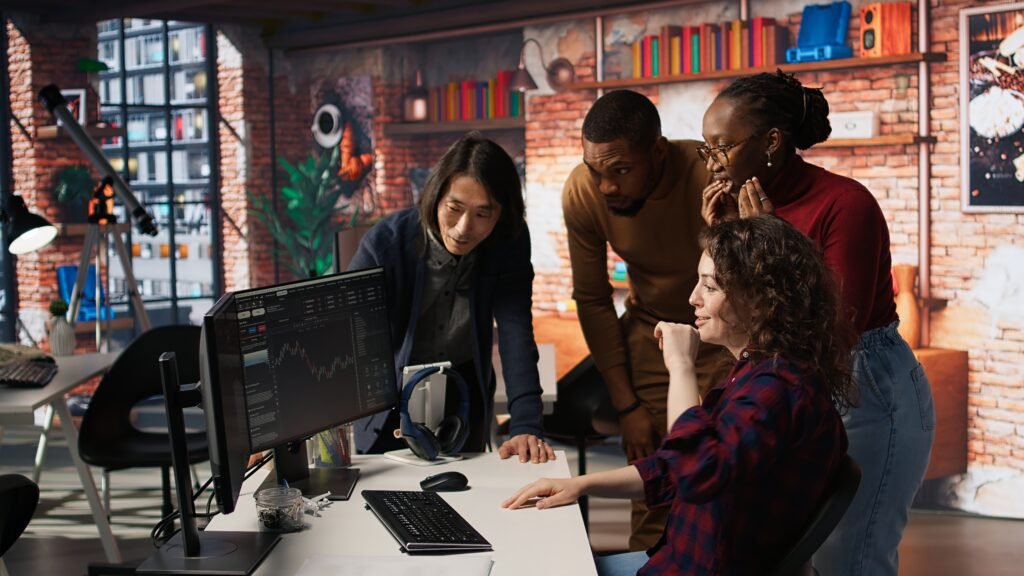 Diverse creative team collaborating around a computer screen in a modern office, analyzing digital data and strategy at a web design agency New York based.